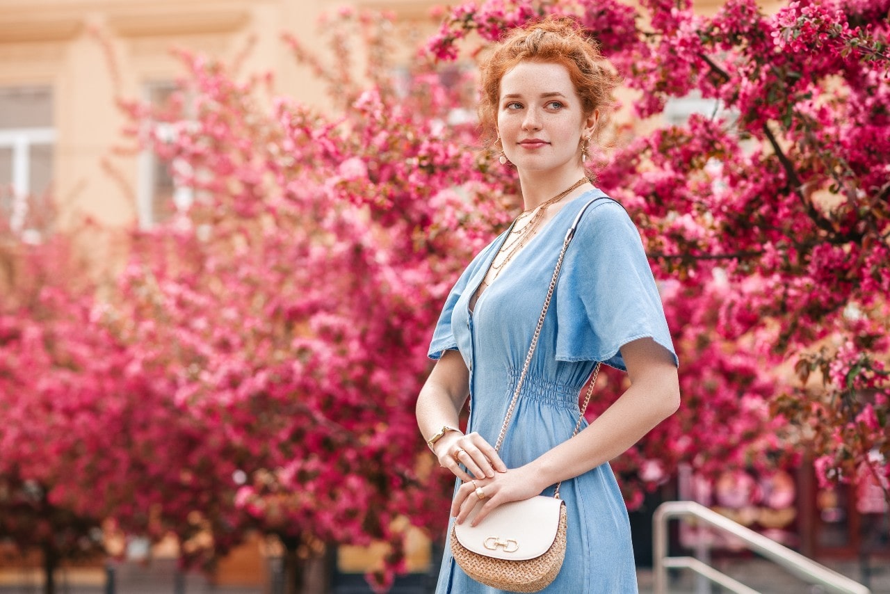 A redheaded woman dressed for a first date waiting outside by pink blooming trees