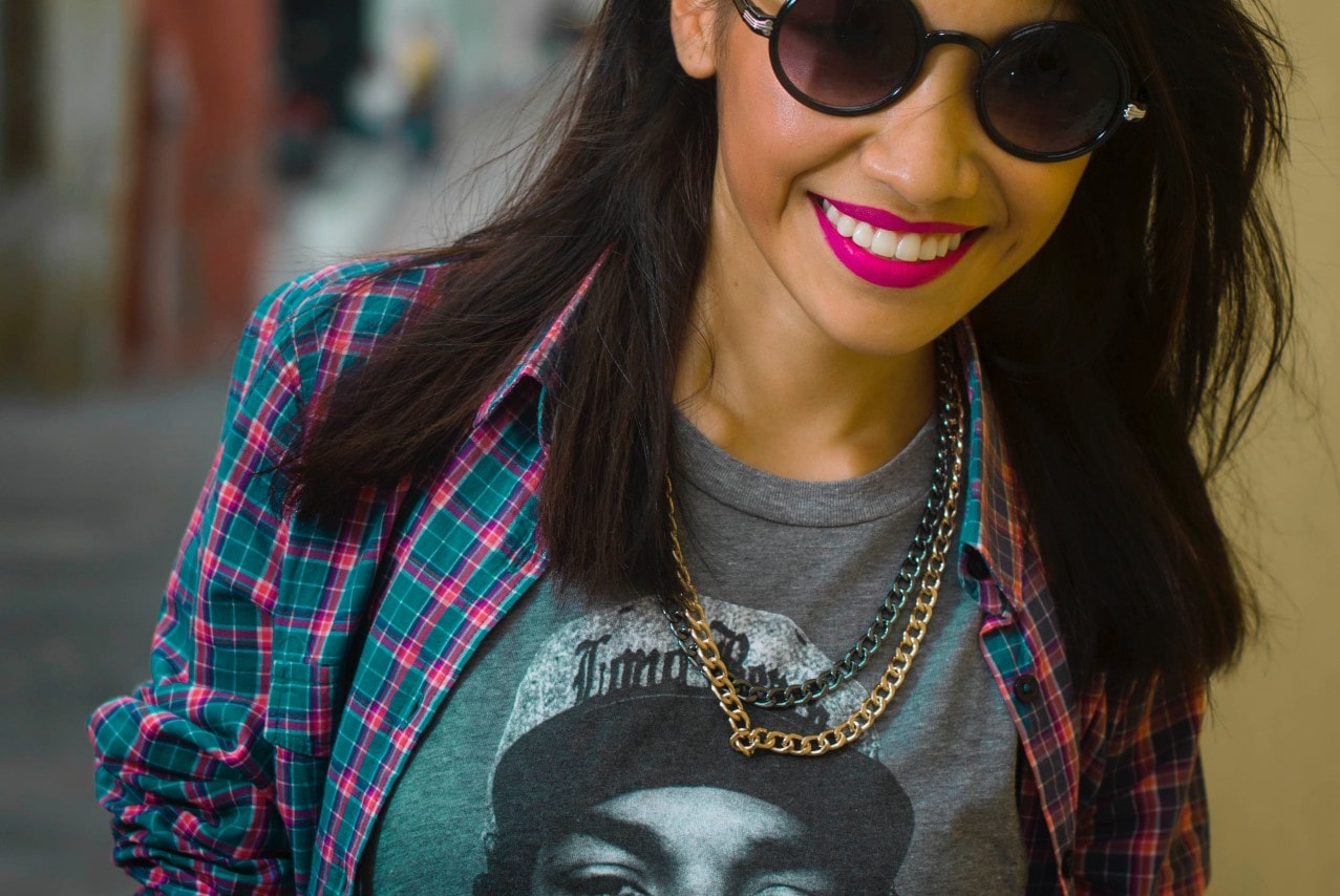 Woman in sunglasses, hot pink lipstick, and flannel plus t-shirt wearing two chain necklaces