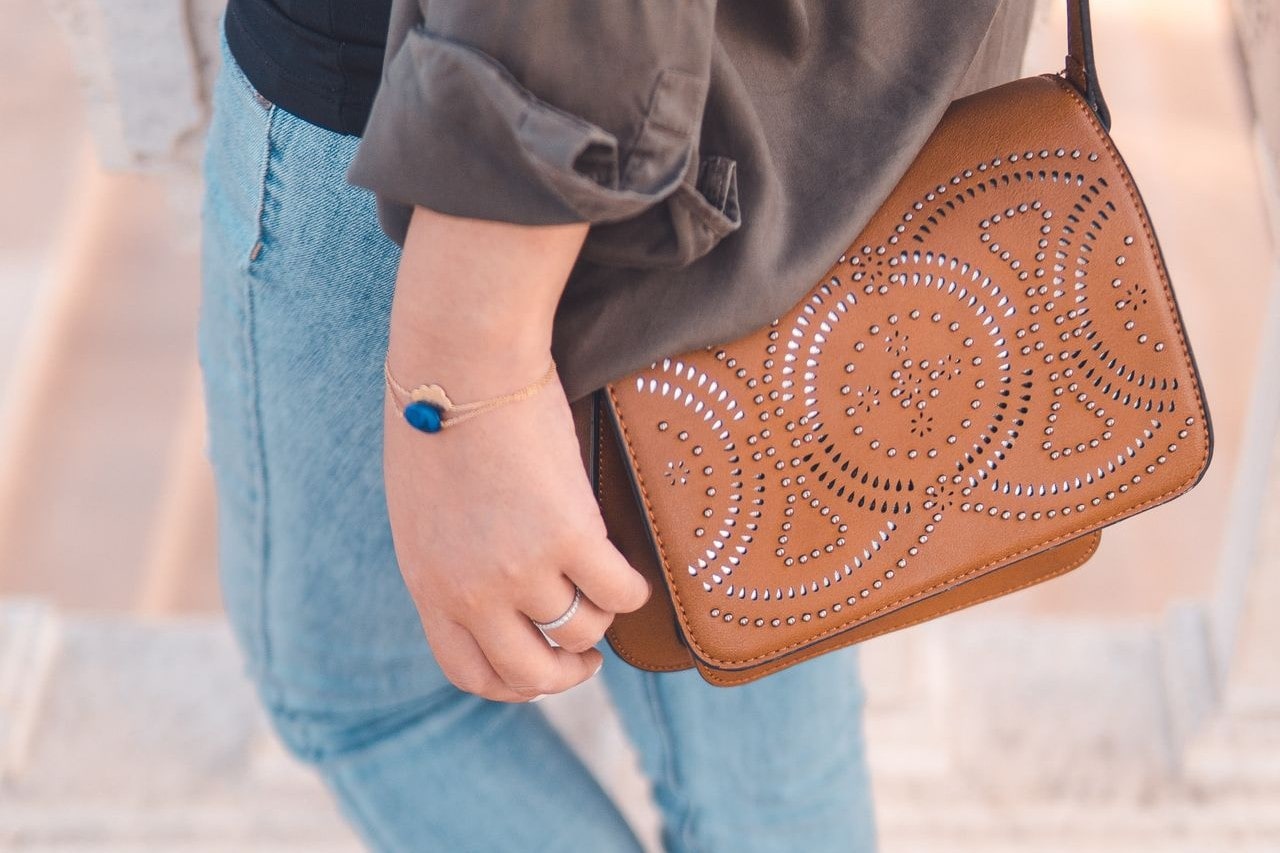 Woman in blue jeans, gray long-sleeve top, and leather purse accessorized with a yellow god and lapis lazuli bracelet plus a white gold and diamond fashion ring