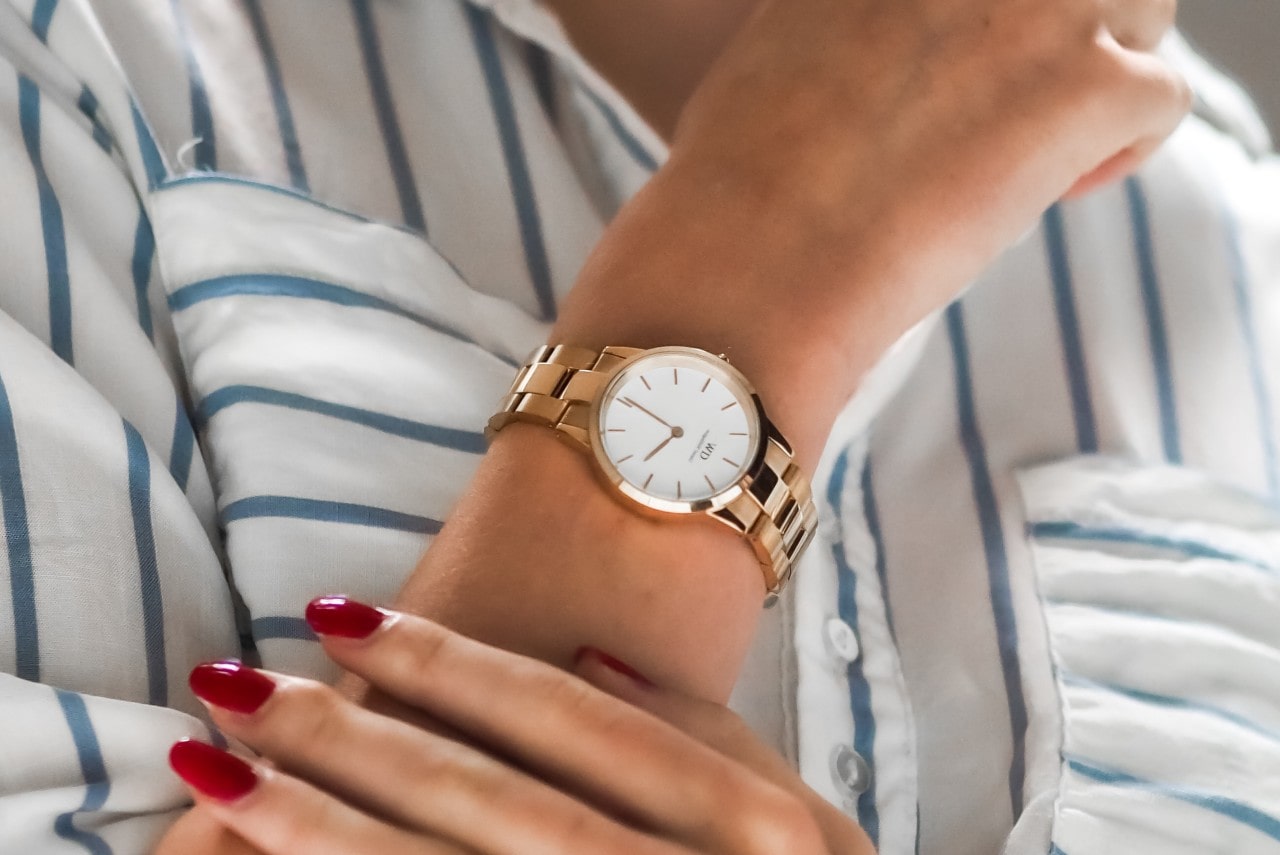Close up image of a woman’s arm crossed over each other, wearing a striped white shirt and a gold and white watch
