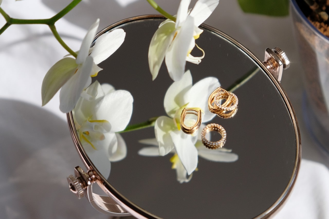 Fashion rings resting on a mirror, looked on by a white orchid