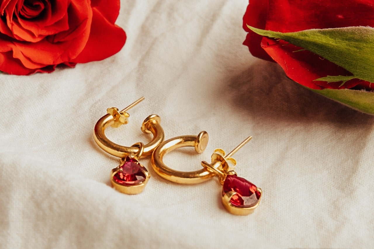 Pair of gold huggies earrings with ruby pendants on a linen surface