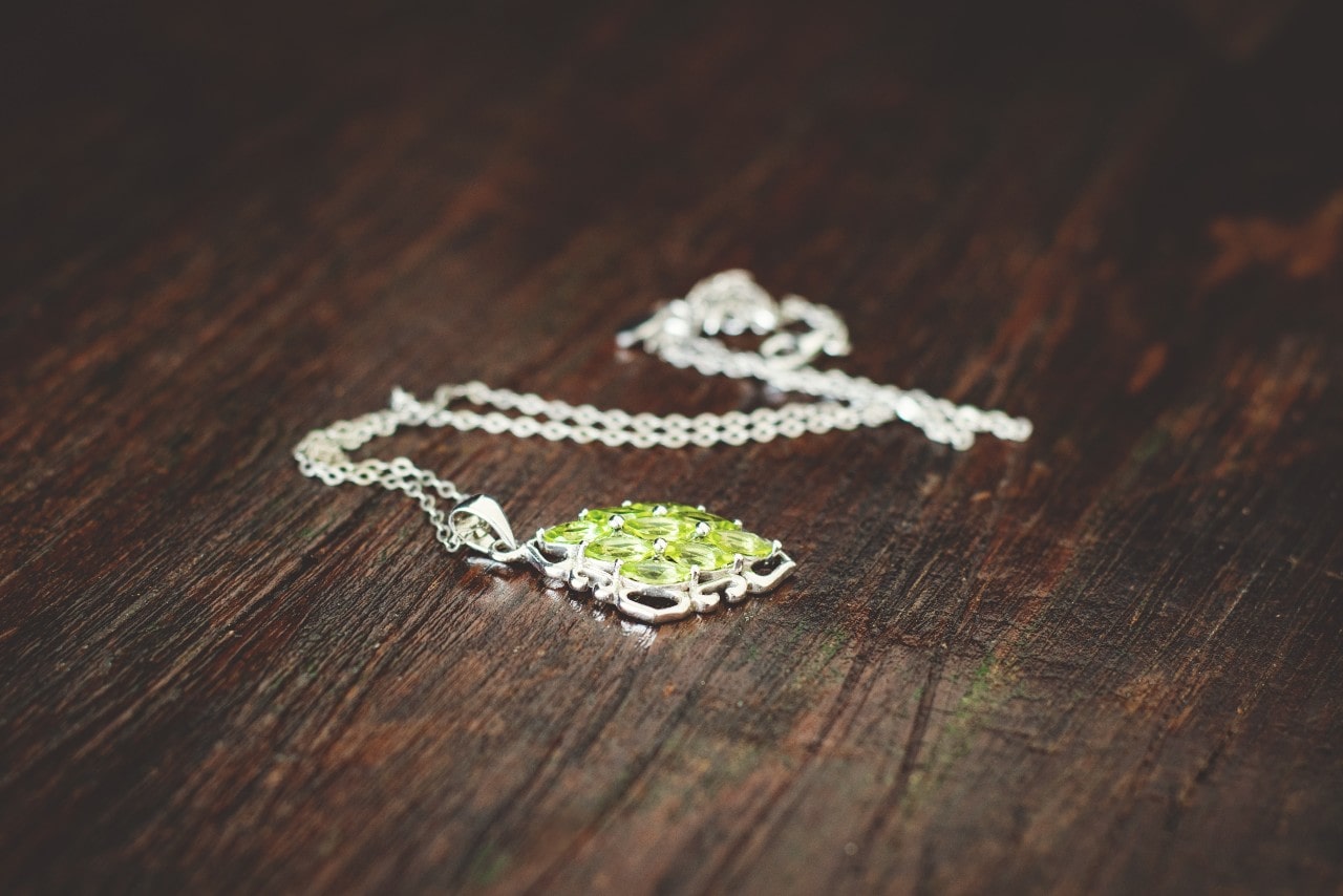 A sterling silver peridot pendant sits on a wooden floor