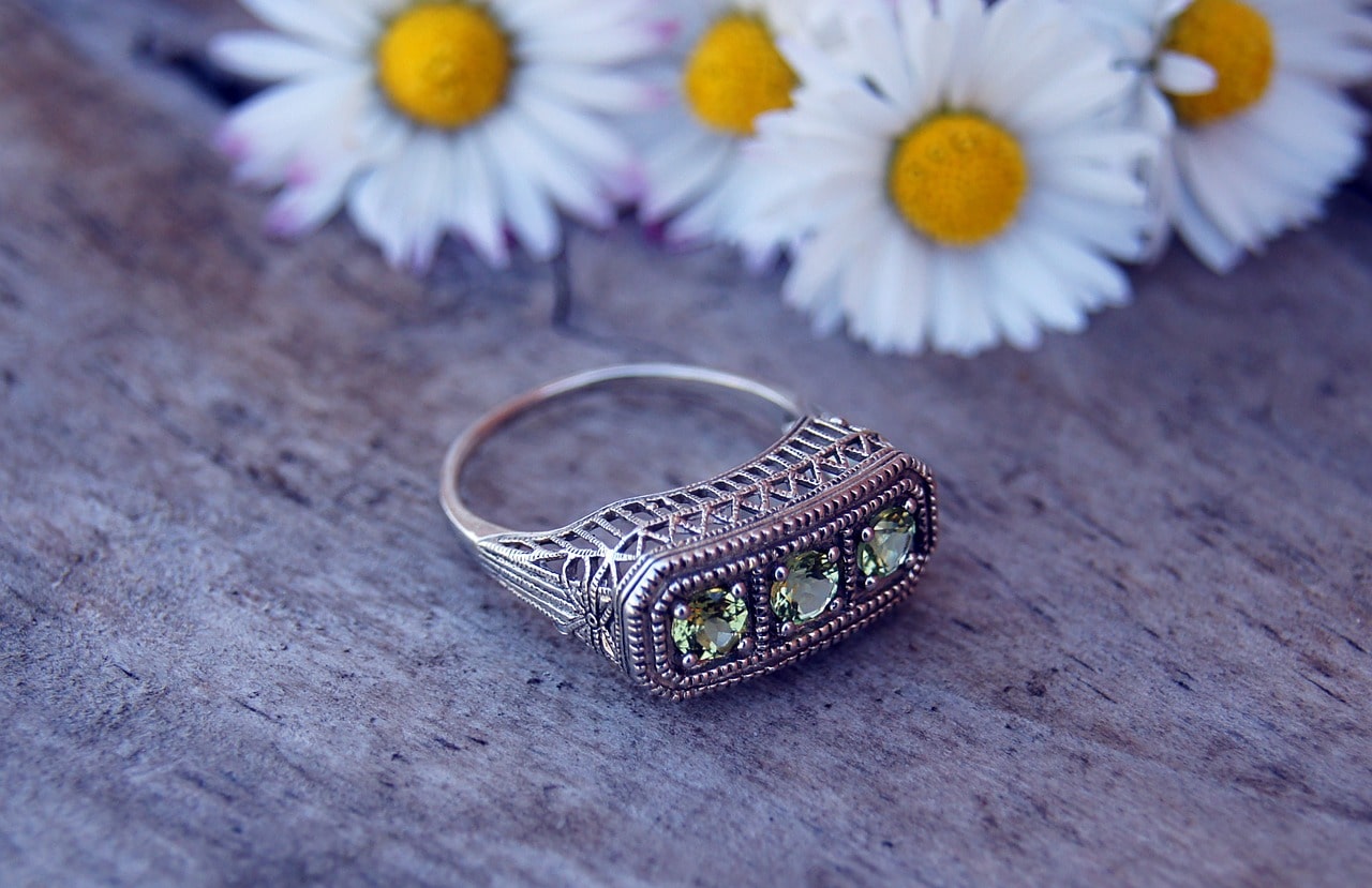 A vintage three-stone peridot fashion ring sits on a wooden surface with daisies