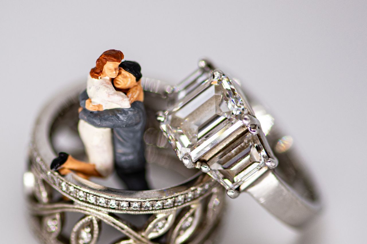 A bride and groom cake topper inside a wedding band with a three stone ring lying on top