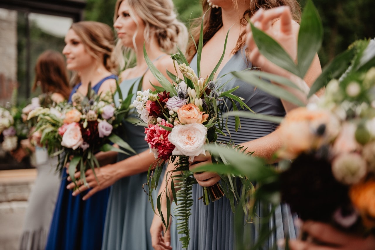 a row of bridesmaids holding their bouquets and wearing dresses in various shades of blue