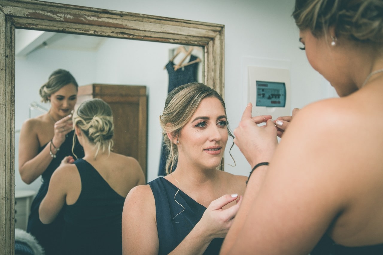 bridesmaids getting ready in front of a mirror, wearing dark blue dresses