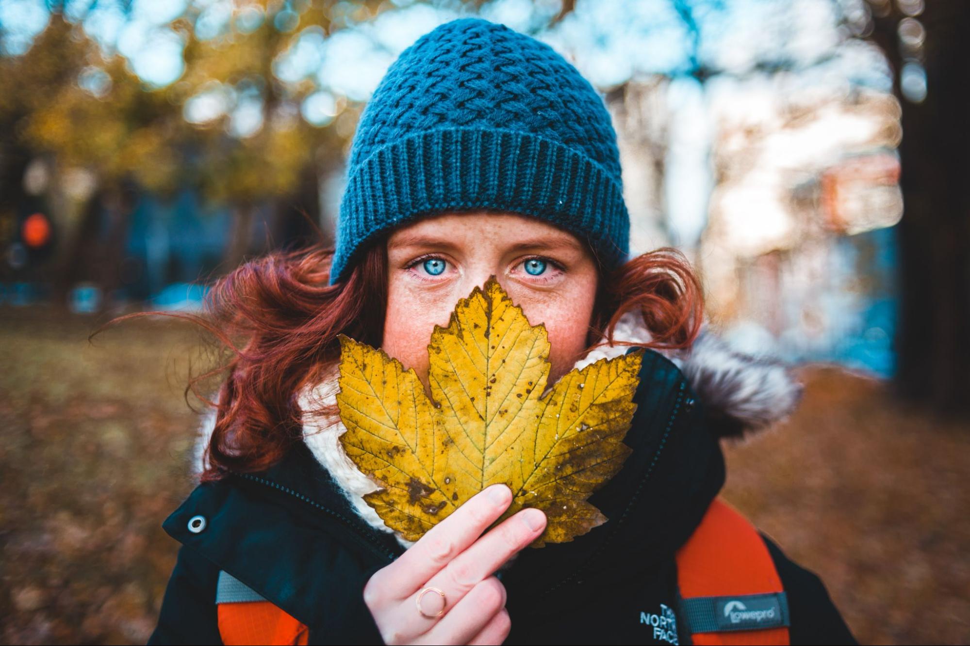 A woman hiking and concealing part of her face with a fall leaf.