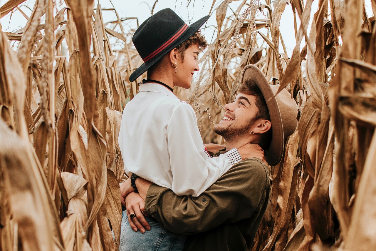 A couple wearing jewelry embrace in a dried cornfield.