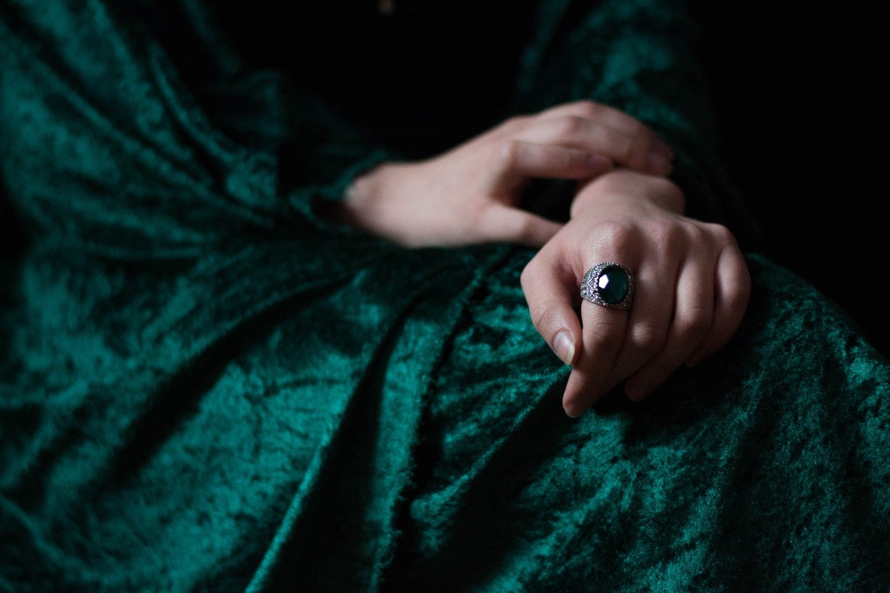 A woman wearing a dark green velvet dress wears a vintage gemstone ring.