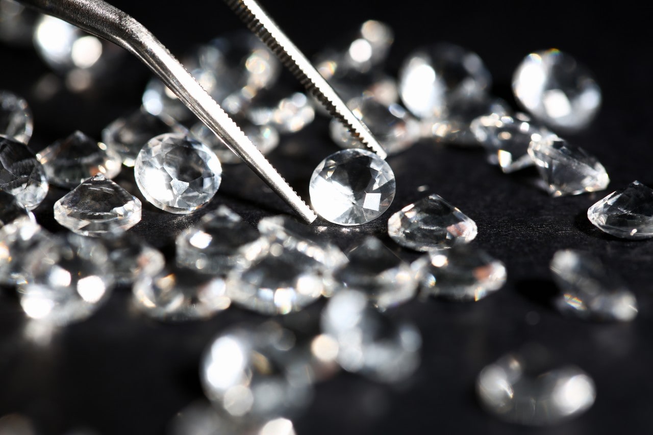 a pair of tweezers picking up a single diamond from a pile of diamonds
