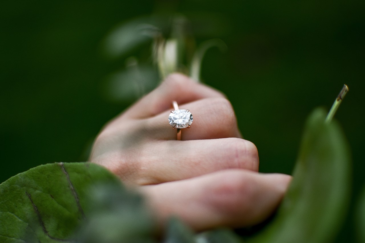 a hand holding a bundle of stems and wearing a rose gold, oval cut engagement ring