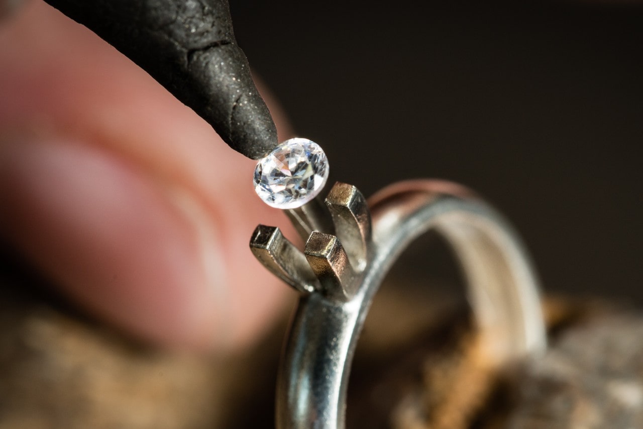 a round cut diamond being placed into a white gold engagement ring setting