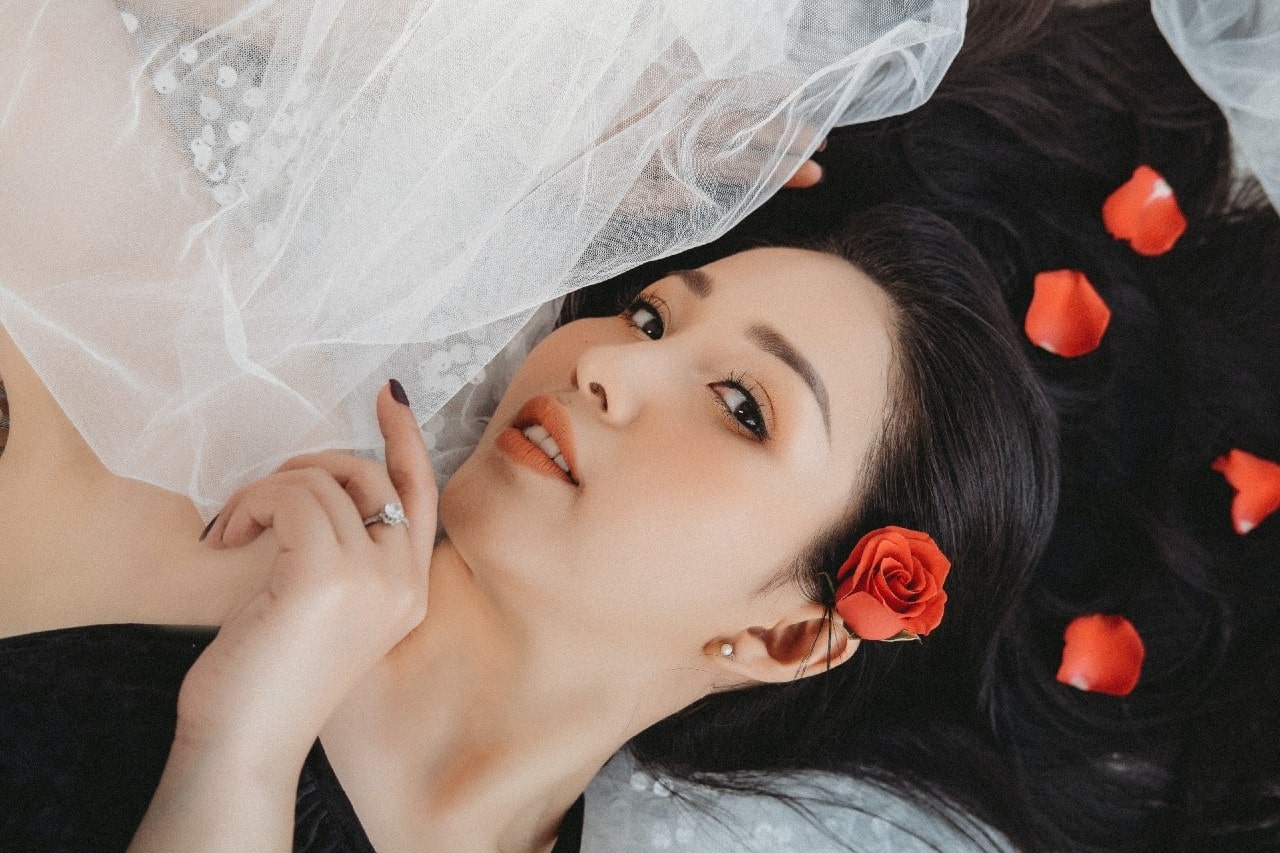lady reclining with flower petals in her hair wearing an engagement ring