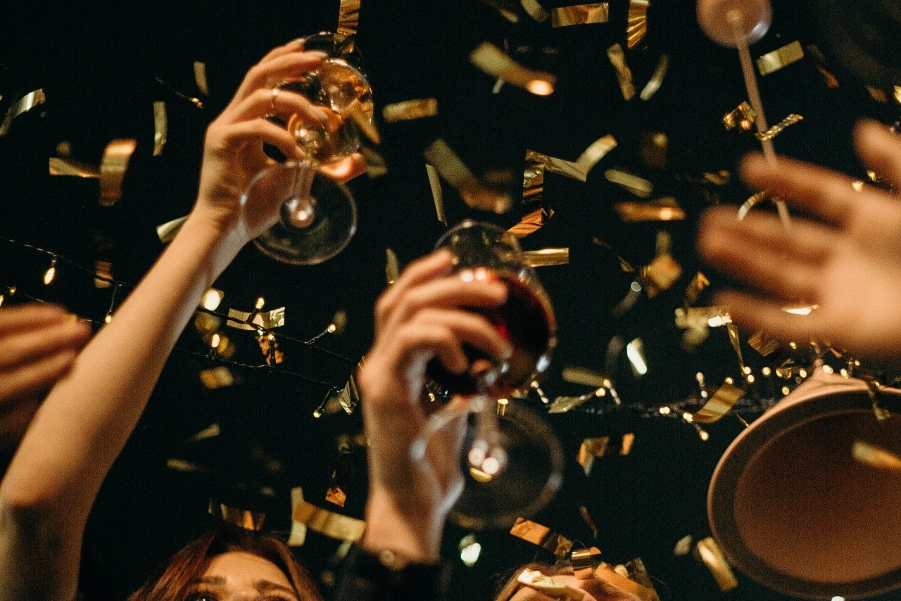 a group raises their wine glasses as gold confetti falls.