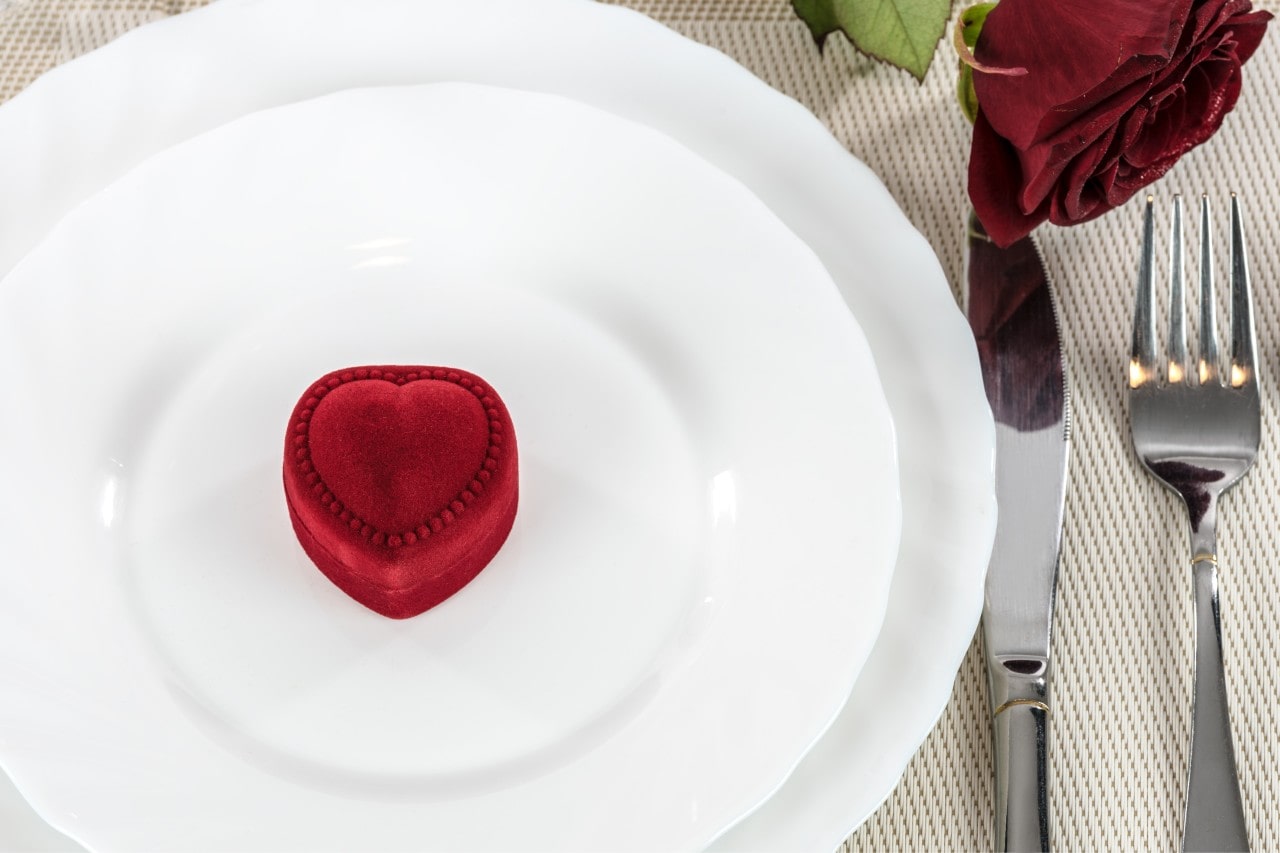 A heart-shaped ring box sits on a dinner plate at a restaurant.