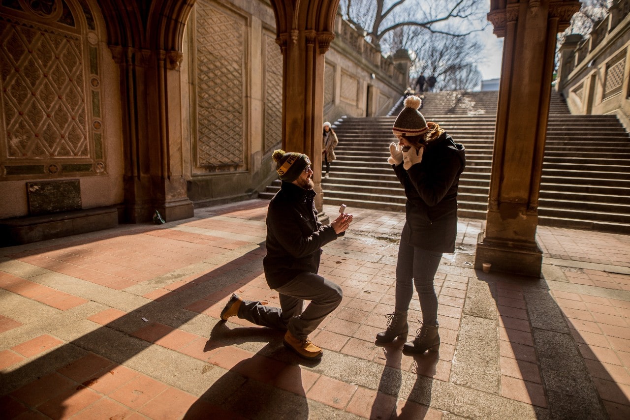 A man proposes to a woman in an ancient plaza.