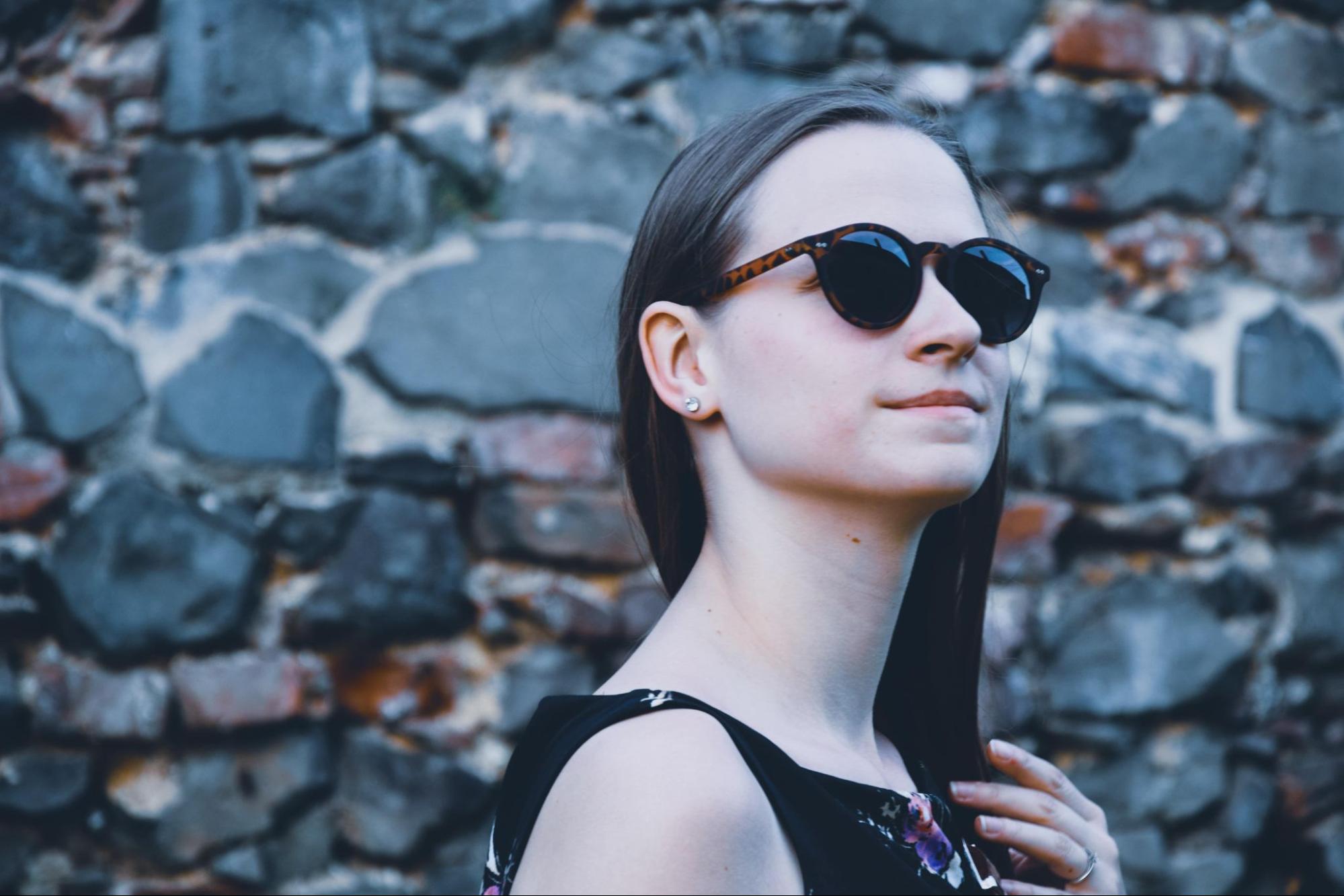 A fashionable young woman wearing diamond stud earrings in front of a stone wall.