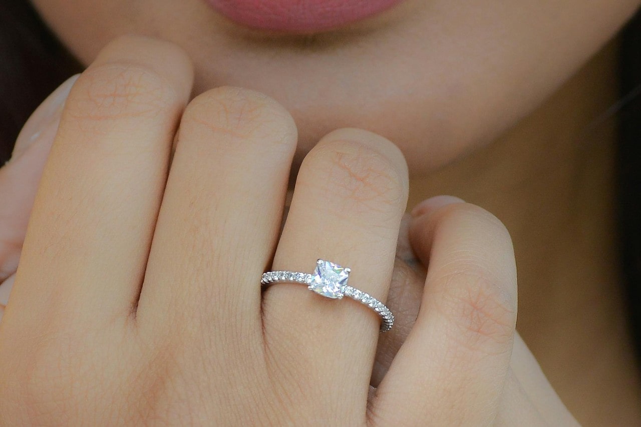 a woman’s hand held up to her face, adorned with a side stone engagement ring