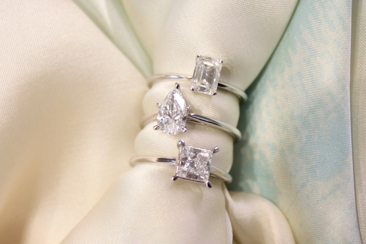 three diamond solitaire engagement rings stacked on a piece of fabric