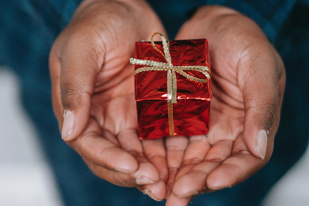 a person’s hands holding a ring box wrapping in red paper