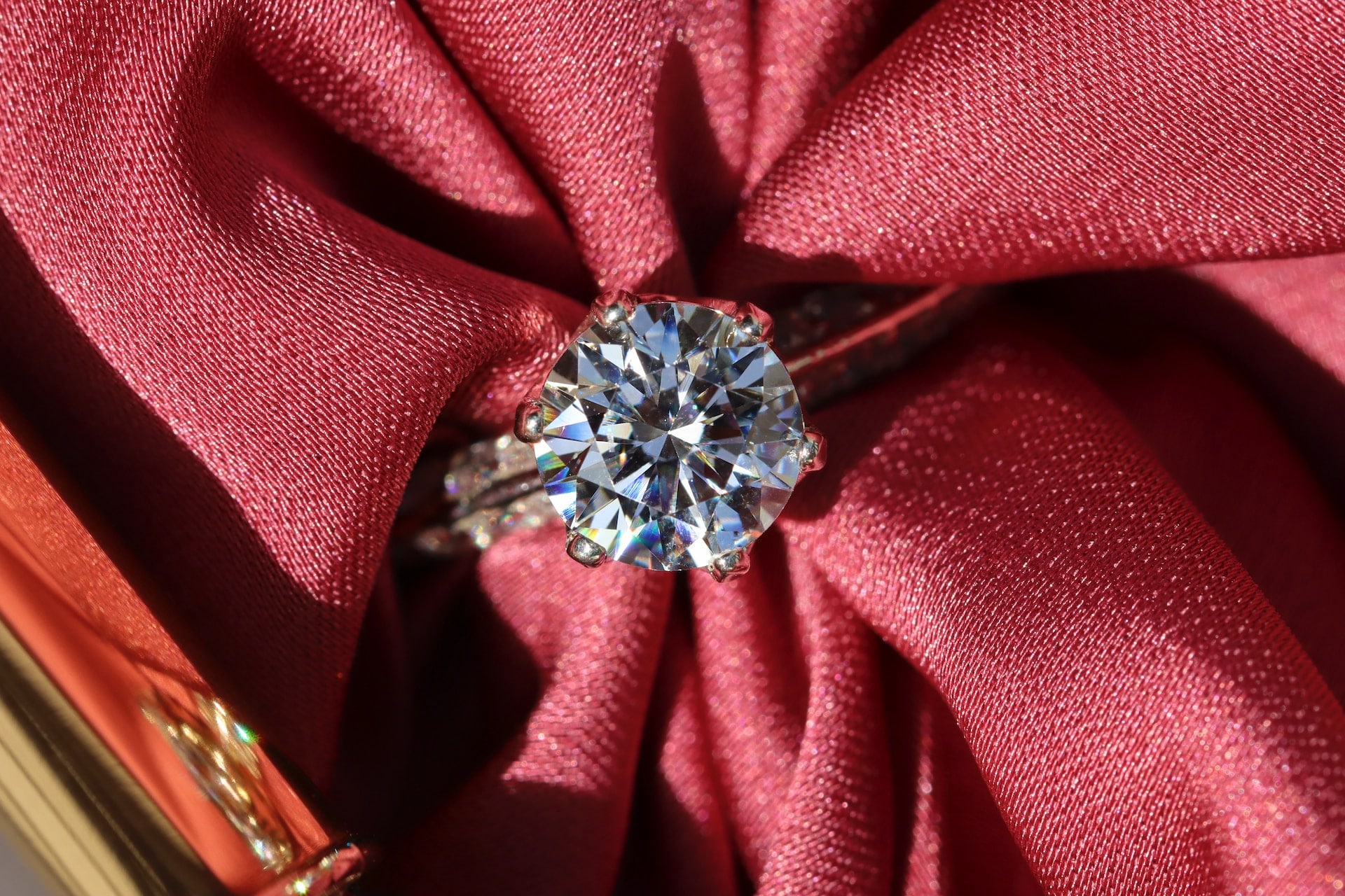 a round cut diamond engagement ring with a piece of red fabric threaded through it