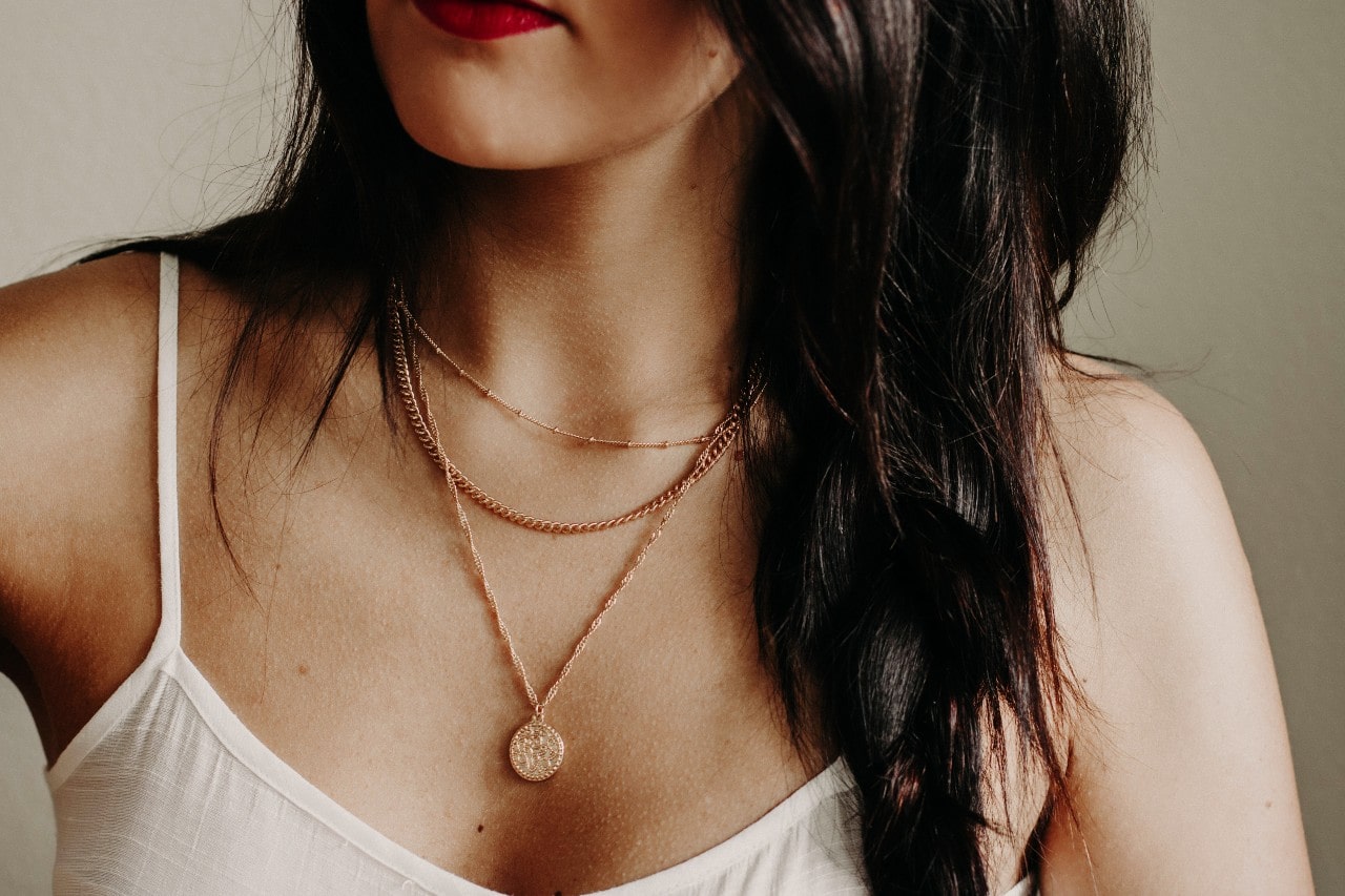 A close-up of a woman wearing layered rose gold necklaces.