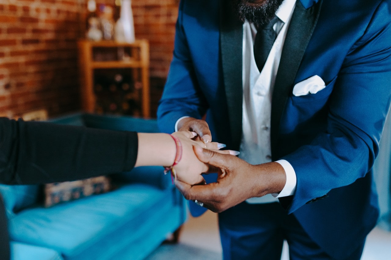 A close-up of a jeweler inspecting a gold band on a customer’s finger.