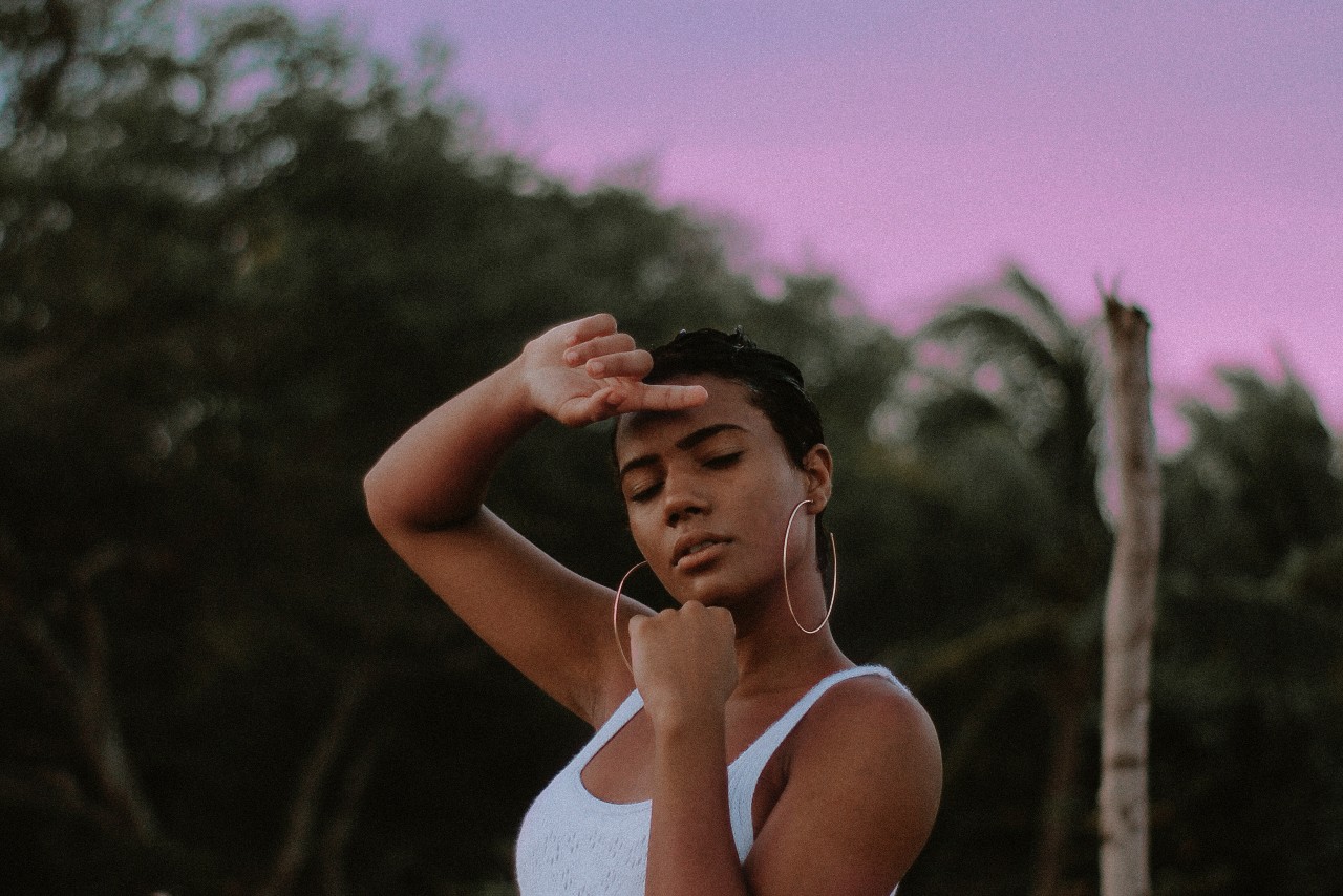 A white shot of a woman wearing bold hoop earrings, striking a pose before palm trees.