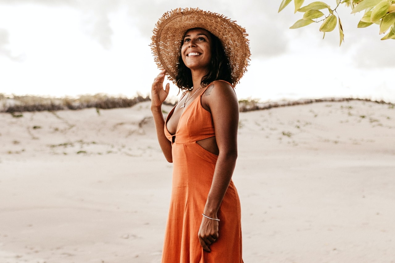 A wide shot of a happy woman wearing gold jewelry at the beach.