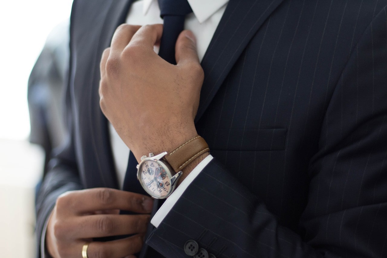 A close-up of a well-dressed man in a suit and luxury watch straightening his tie. A close-up of a well-dressed man in a suit and luxury watch straightening his tie.