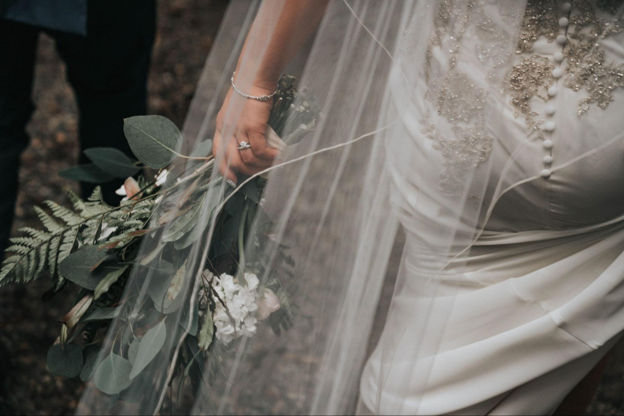 A bride walks away with her bouquet, wearing a solitaire ring and diamond band.