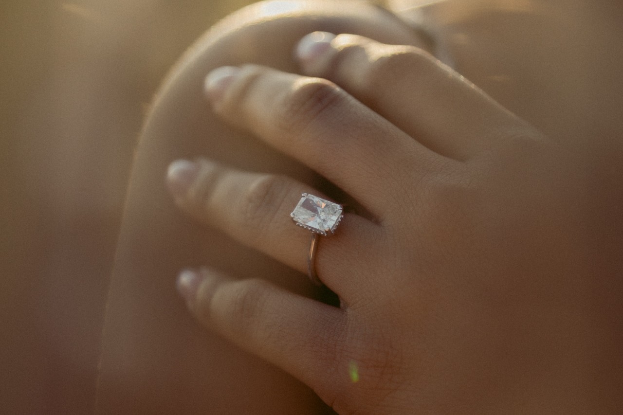 a woman’s hand on her shoulder, wearing a solitaire, emerald cut engagement ring