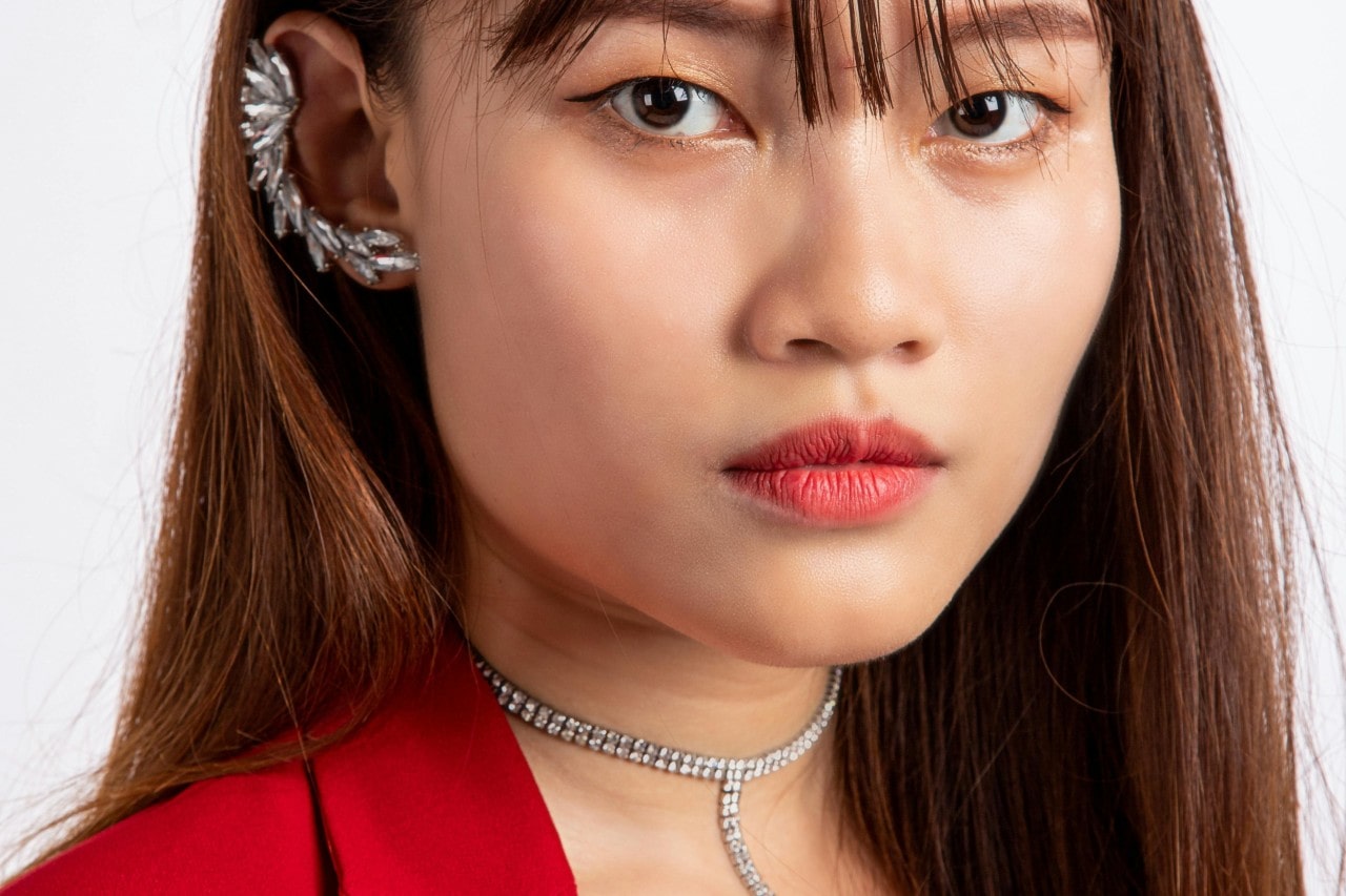 A close-up of a woman wearing distinctive earrings and a diamond necklace.