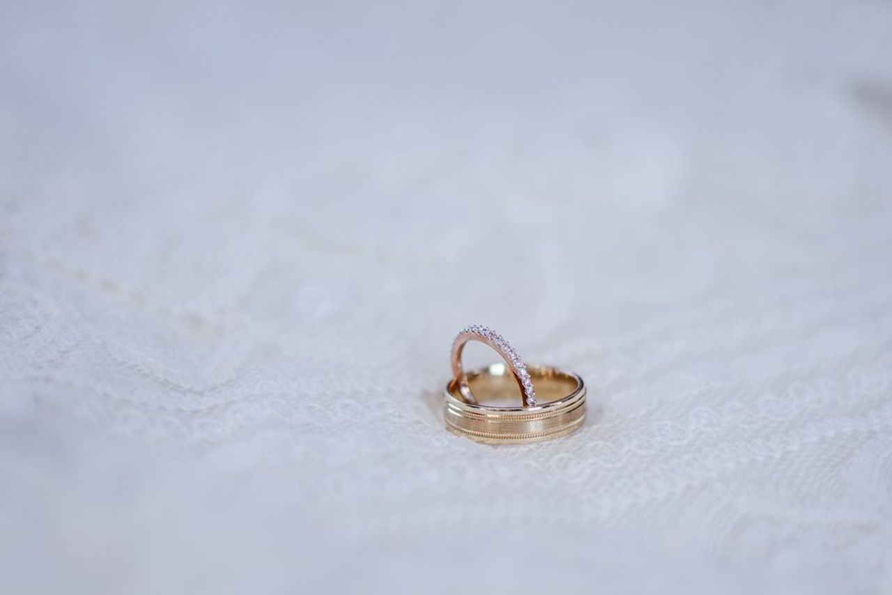 A matching men’s wedding band and women’s band sit on a lace fabric.