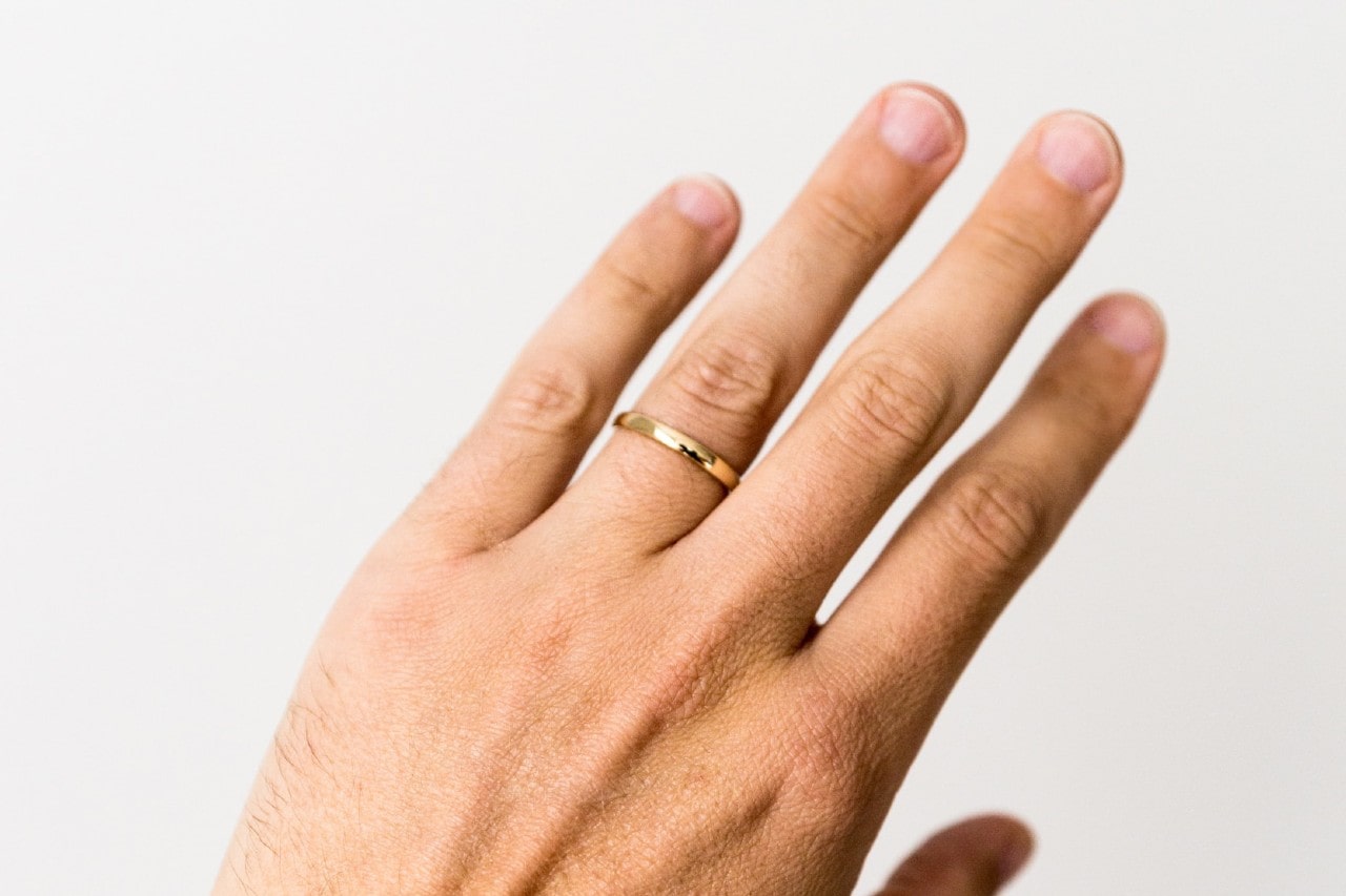 A close-up of a man’s hand wearing a simple gold wedding ring.