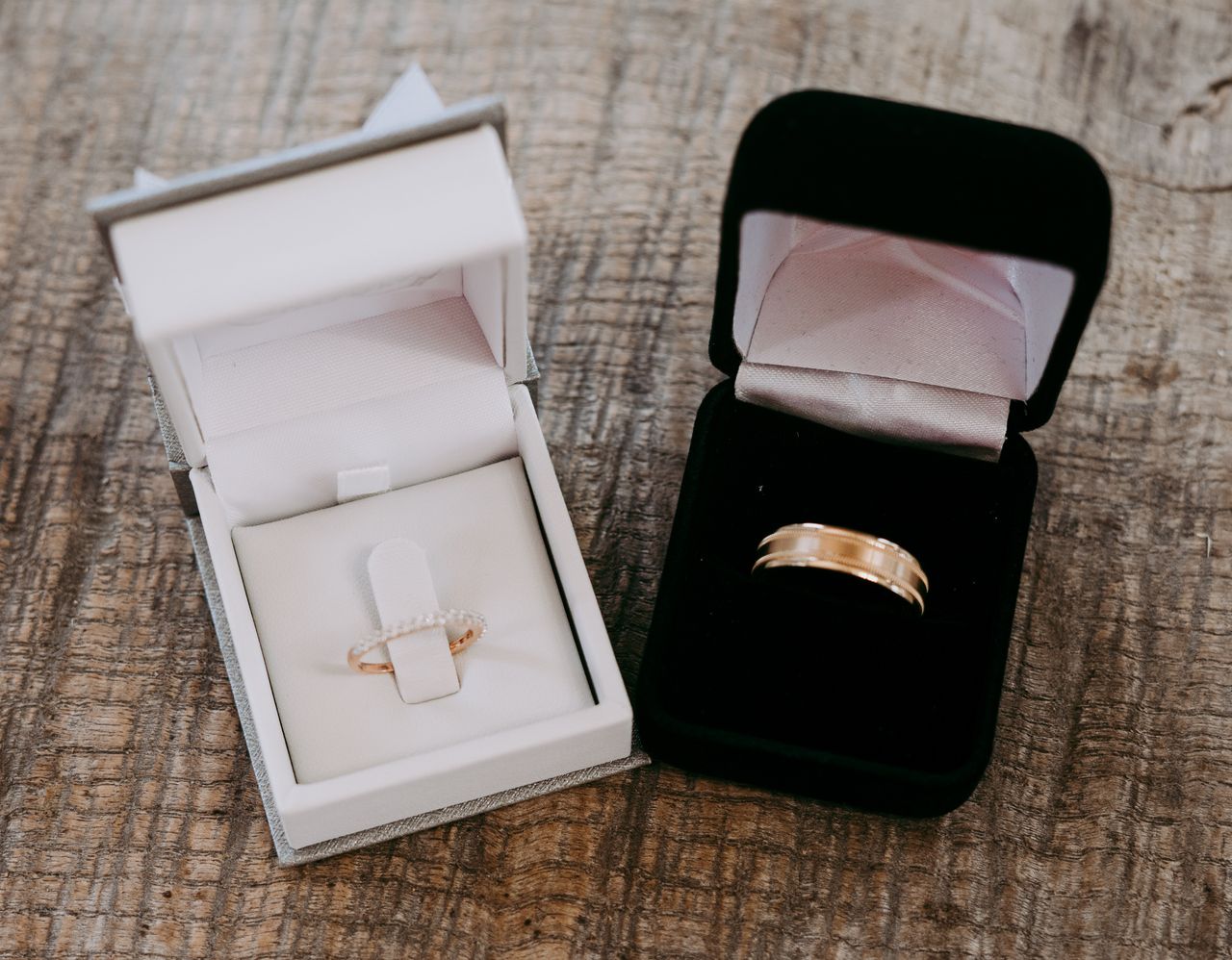 A close-up of a men’s gold wedding band displayed in-box next to a side stone women’s band.