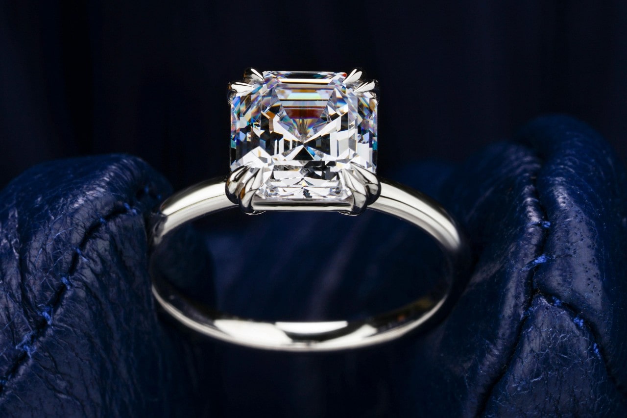 close up image of a princess cut engagement ring between gloved fingers