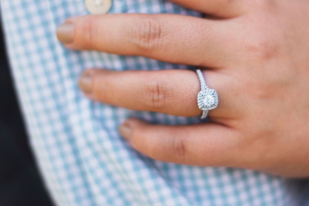 a woman’s hand resting on a plaid sleeve, wearing a white gold halo engagement ring