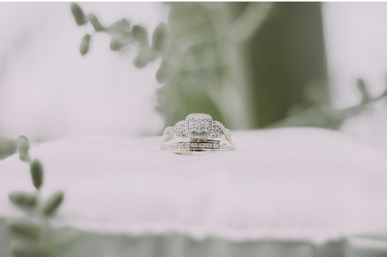 A unique engagement ring and matching wedding band sitting on a white pillow.